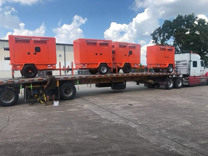 Row of AMCO enclosed pump units loaded on a flatbed trailer for delivery